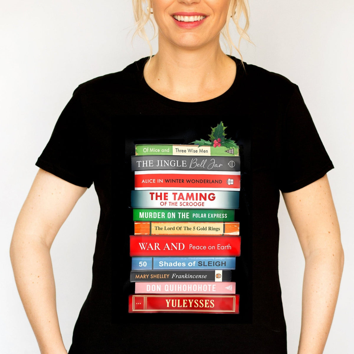 Person wearing a black Christmas t-shirt with book stack design and puns on famous book titles on a white background