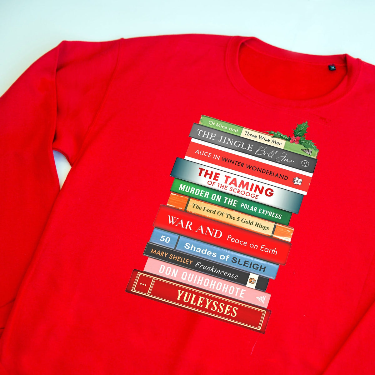 Red christmas sweatshirt with a graphic of books stacked on a white background
