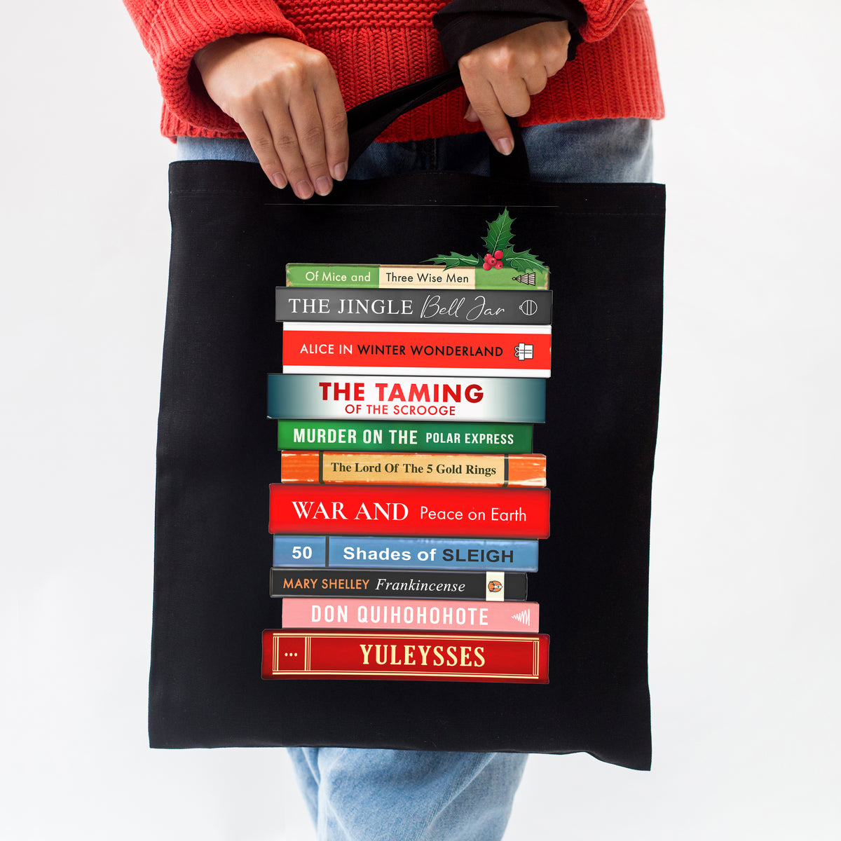 Black tote bag with book title design held by a person wearing a red sweater.