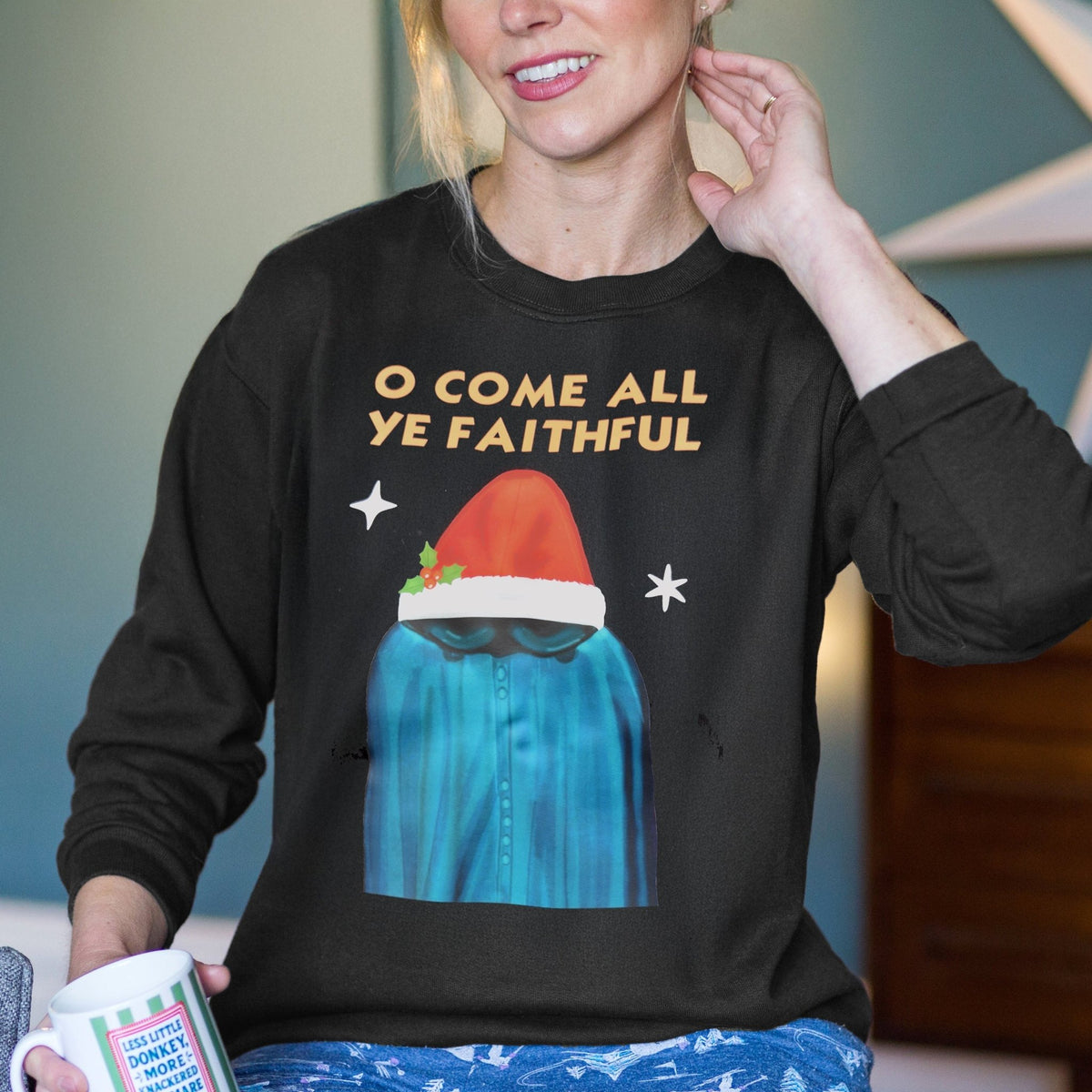 Person wearing a black sweater with a Christmas-themed Traitors TV show design and holding a mug.