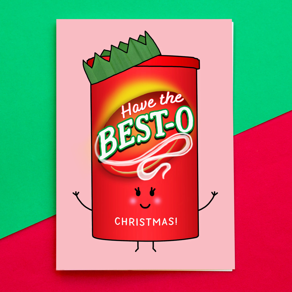 A square greeting card featuring a cartoon red can character with the text 'Have the BEST-O CHRISTMAS!' on a pink card, photographed against a split green and red background.