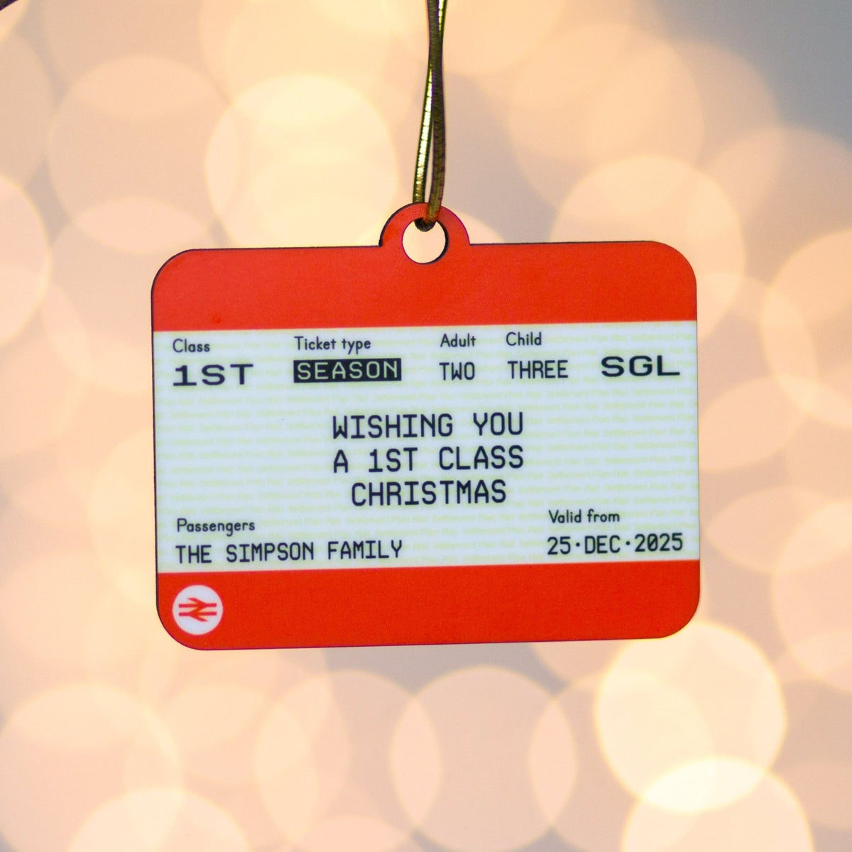 Orange and white Christmas ornament resembling a National Rail train ticket with festive text on a blurred light background.