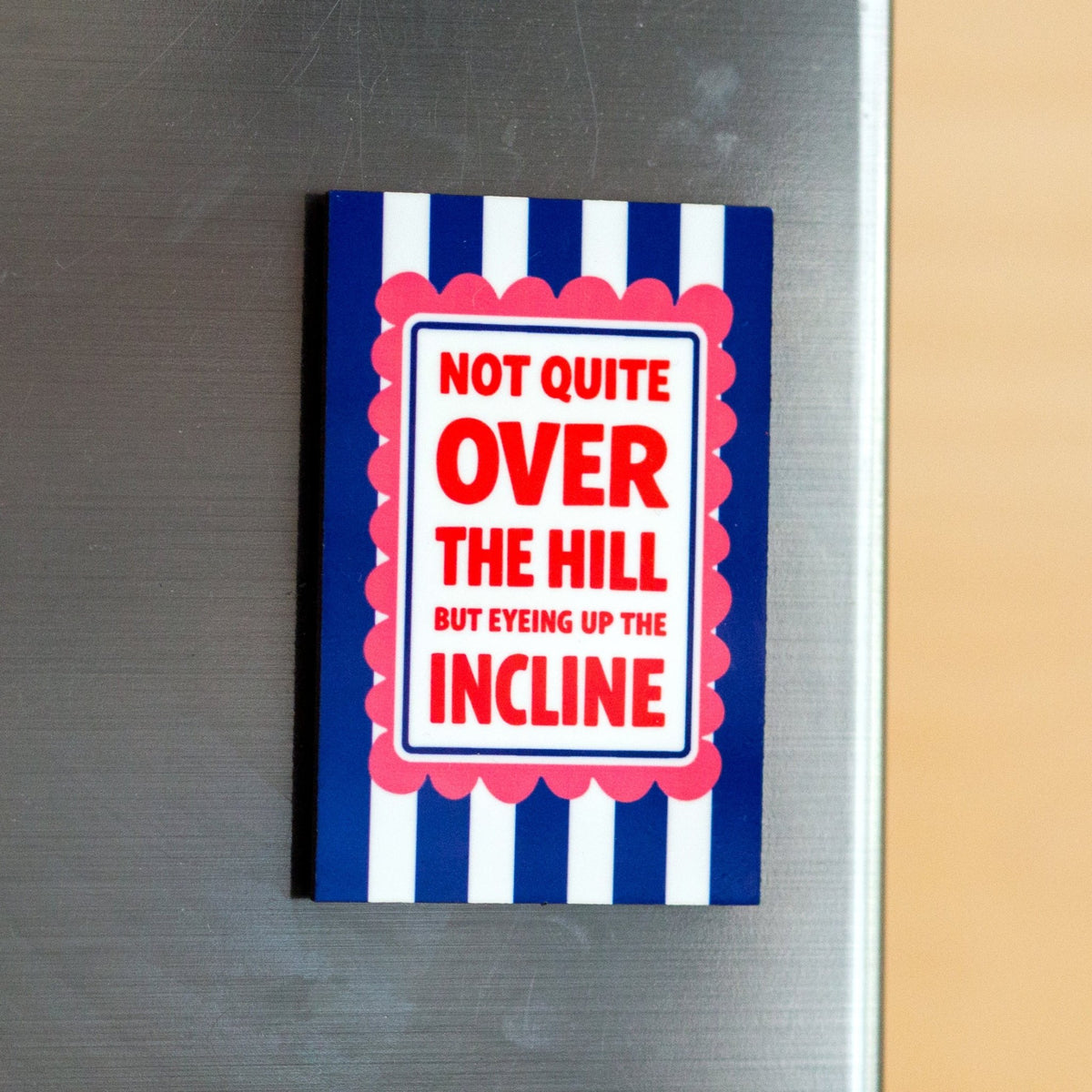 Fridge magnet with blue and white striped cover and red text on a metallic surface.