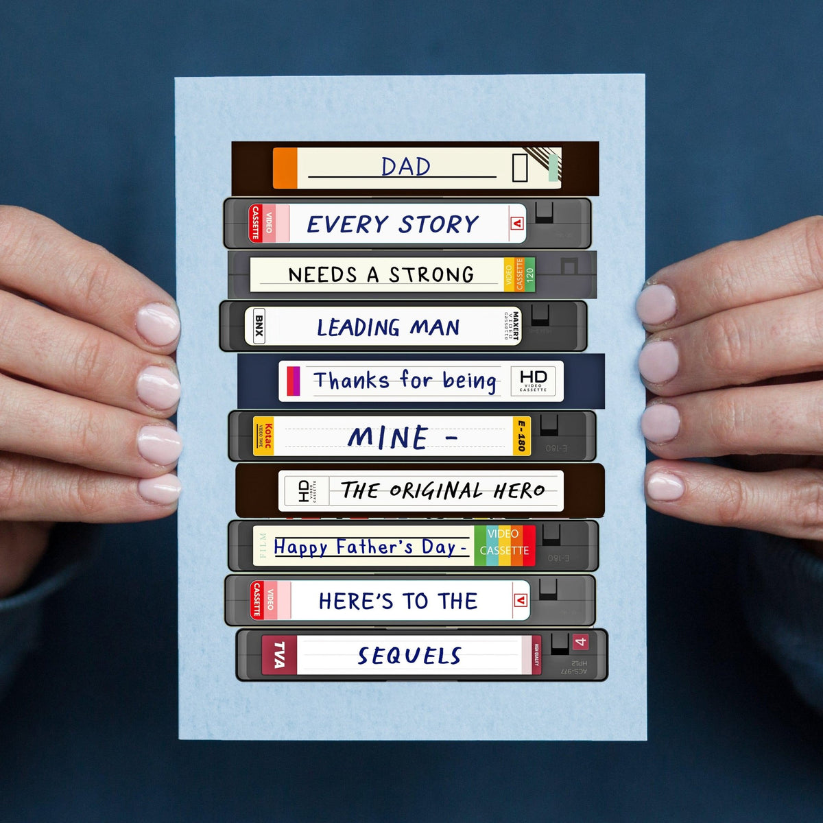 fathers day card featuring a stack of VHS tapes that spell out a message about dad being your original ero. Pictured in hands against a blue jumper