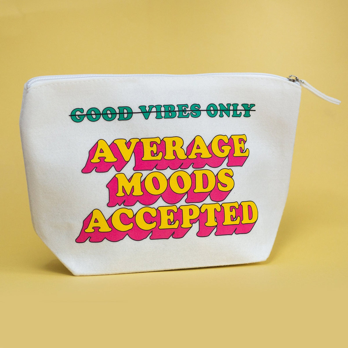A white canvas zippered pouch with retro-style text reading 'GOOD VIBES ONLY AVERAGE MOODS ACCEPTED' in green, yellow, and pink, set against a solid pale yellow background.