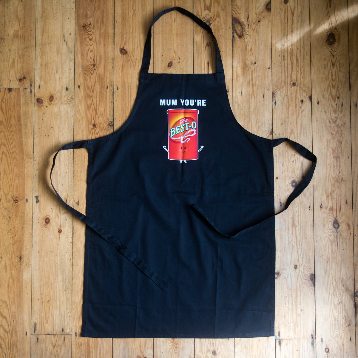 black apron for mums with best mum slogan laid on a wooden floor