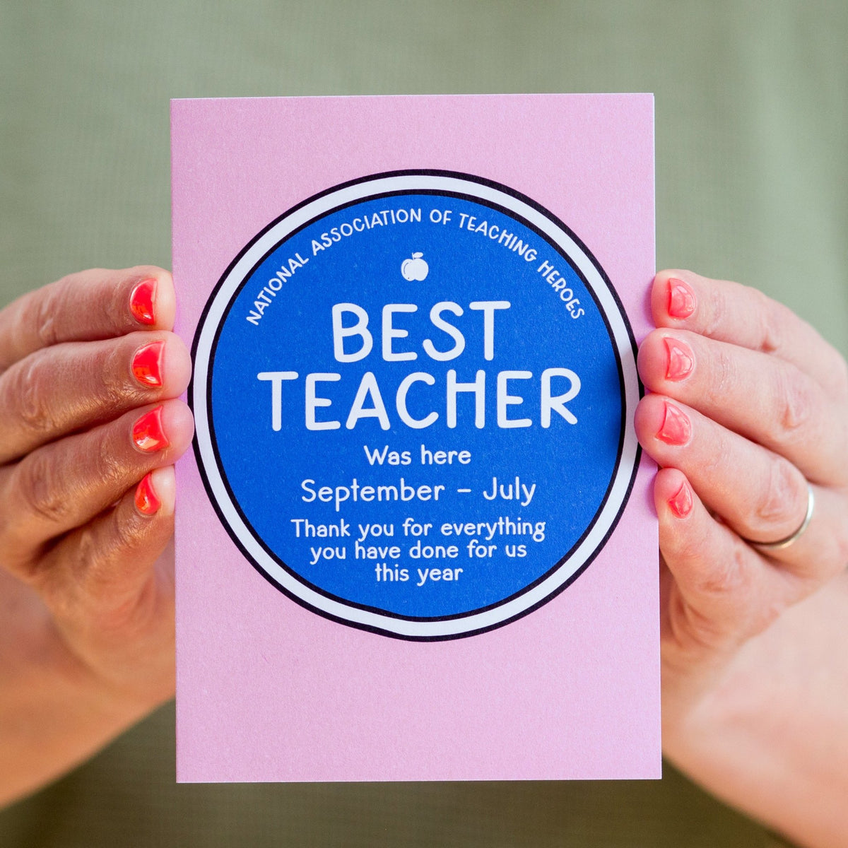 Card with 'Best Teacher' message held by two hands against a green background