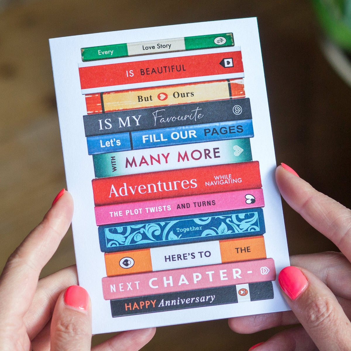 Card with colorful text and book design held by hands on a wooden surface