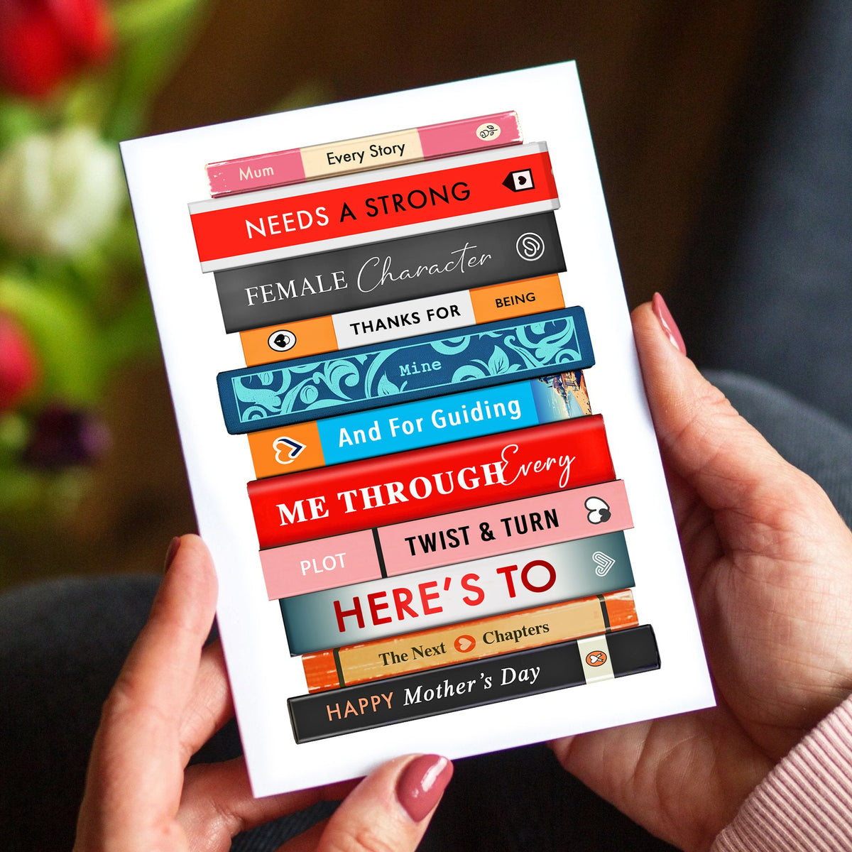 hands holding a mother's day card featuring a stack of books and flowers in the background