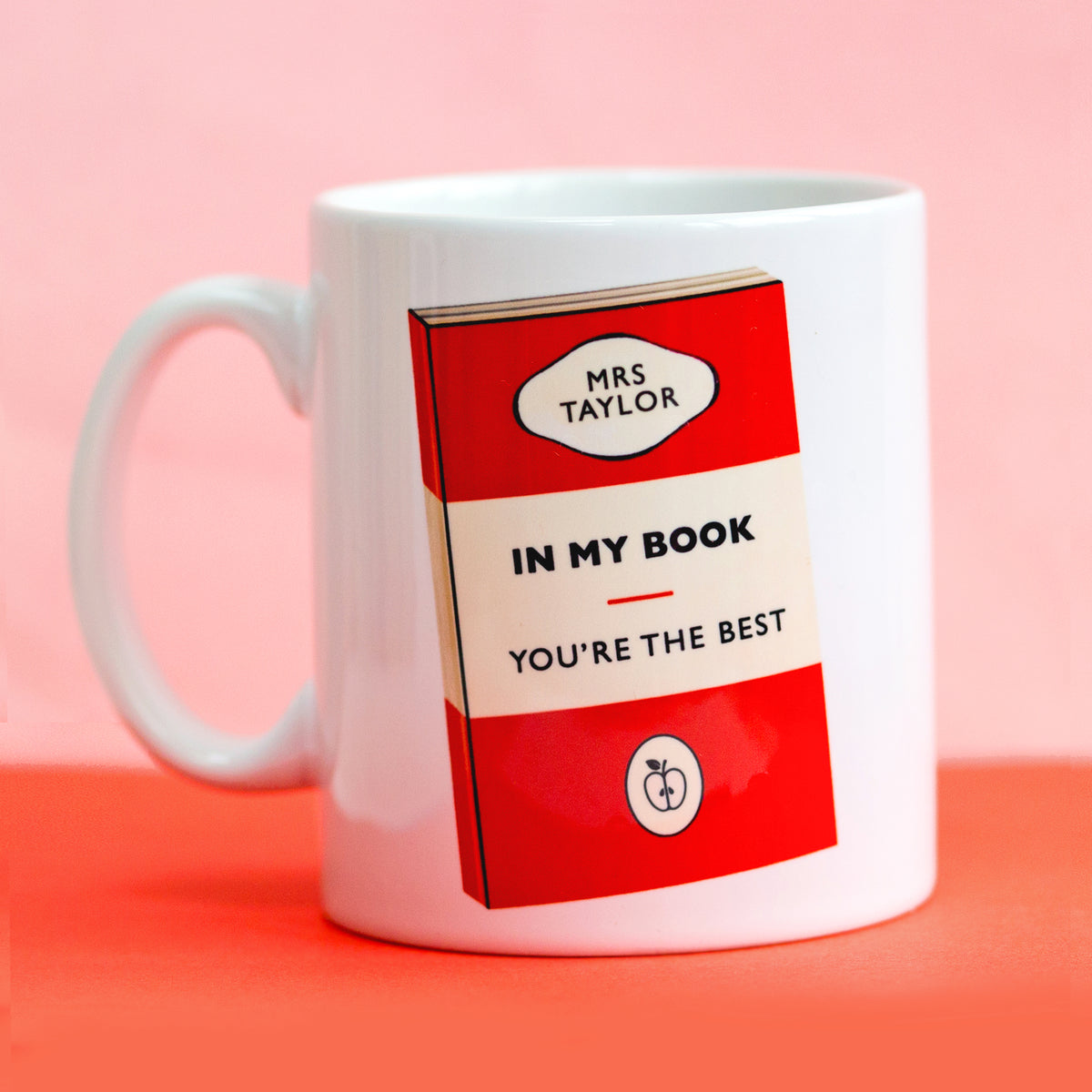 White mug for a teacher with a book-themed design on a pink background