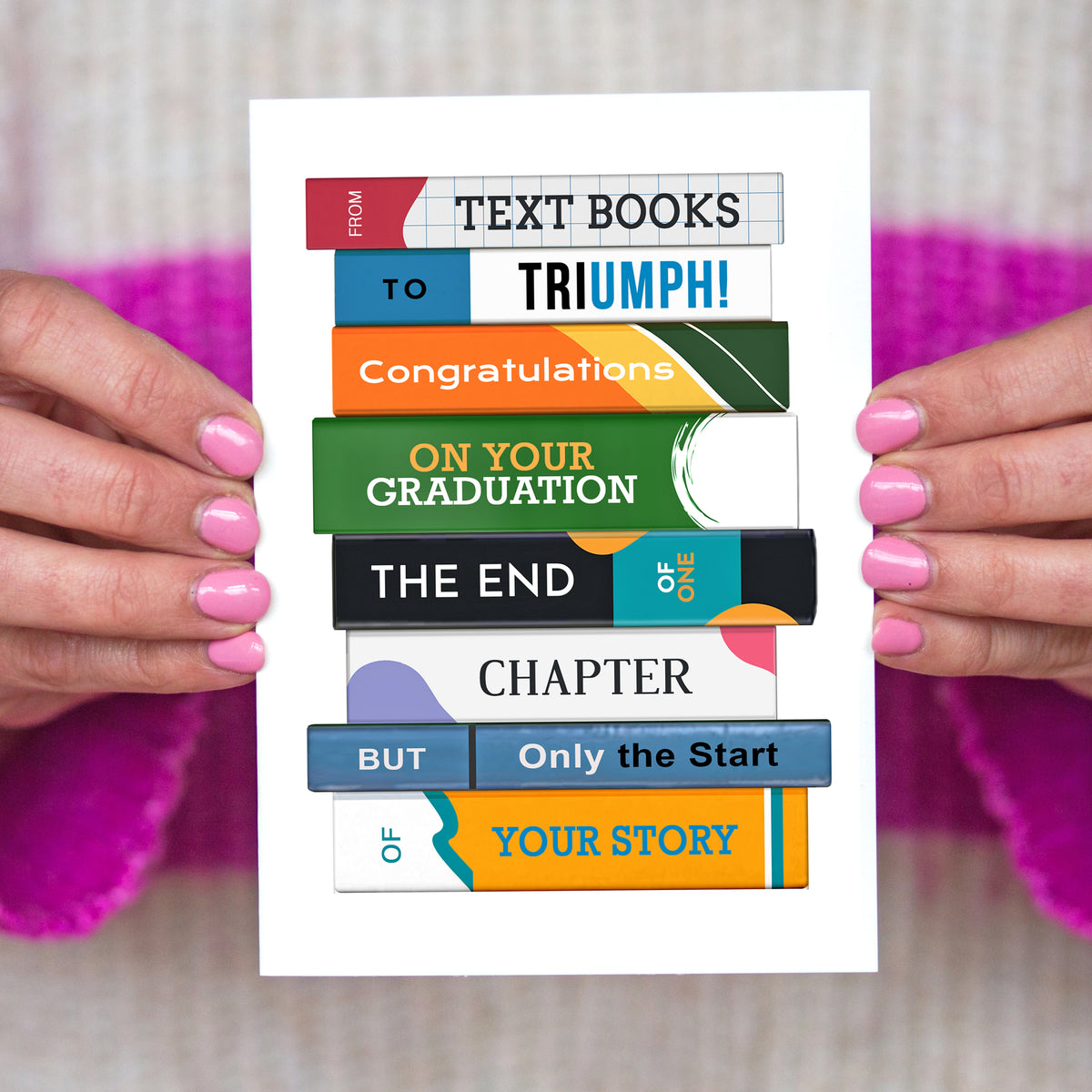Graduation card with colorful book design held by hands against a blurred background
