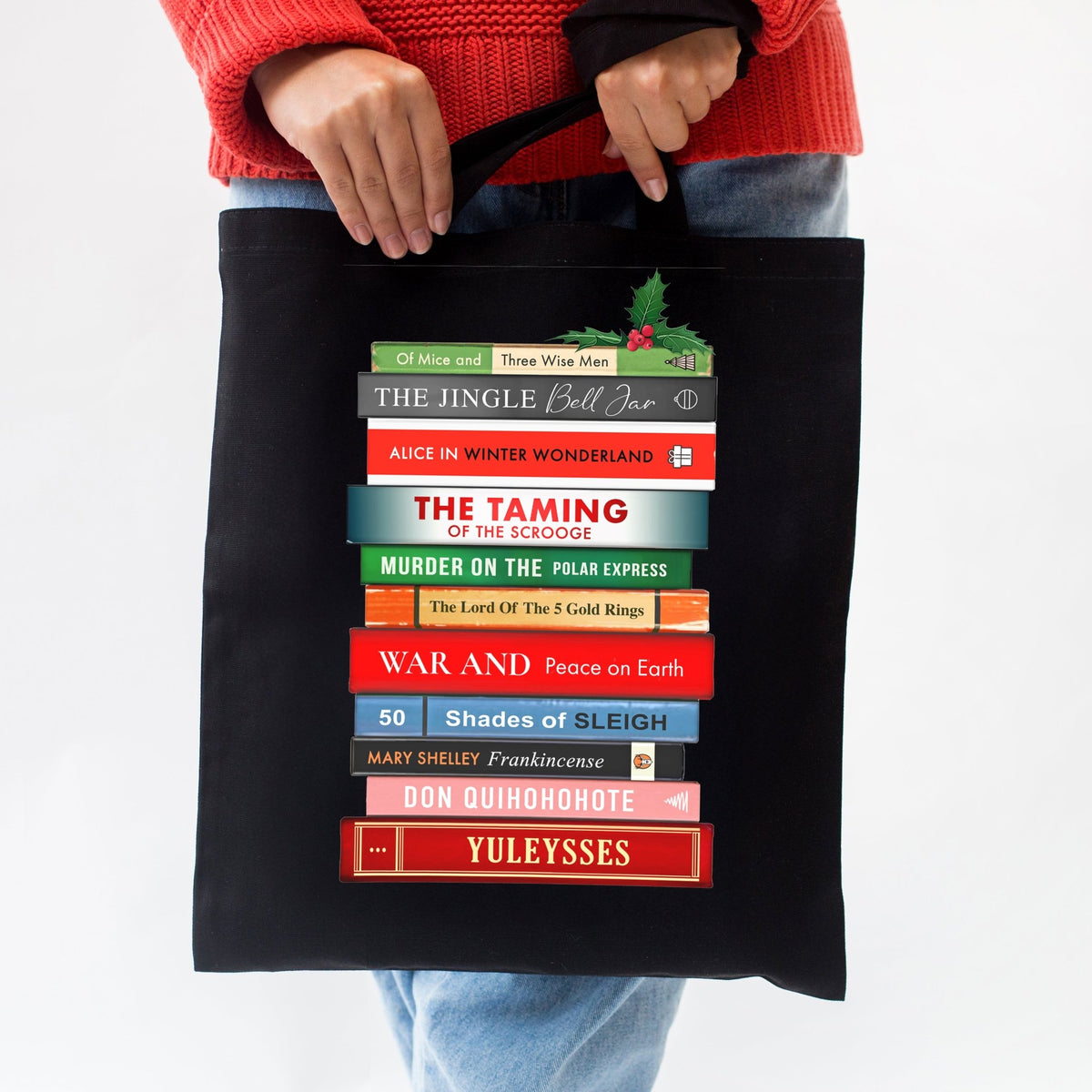 Black tote bag with book title design held by a person wearing a red sweater.