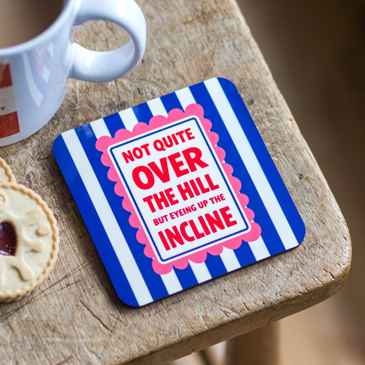 Coaster with humorous text on a wooden surface with a mug and cookie.