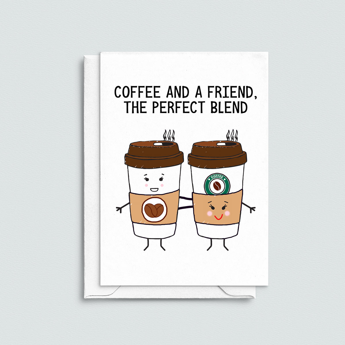 A white greeting card with a black text reading 'COFFEE AND A FRIEND, THE PERFECT BLEND' above two cartoon takeaway coffee cups holding hands. The card is shown standing upright with a white envelope behind it on a light gray background.