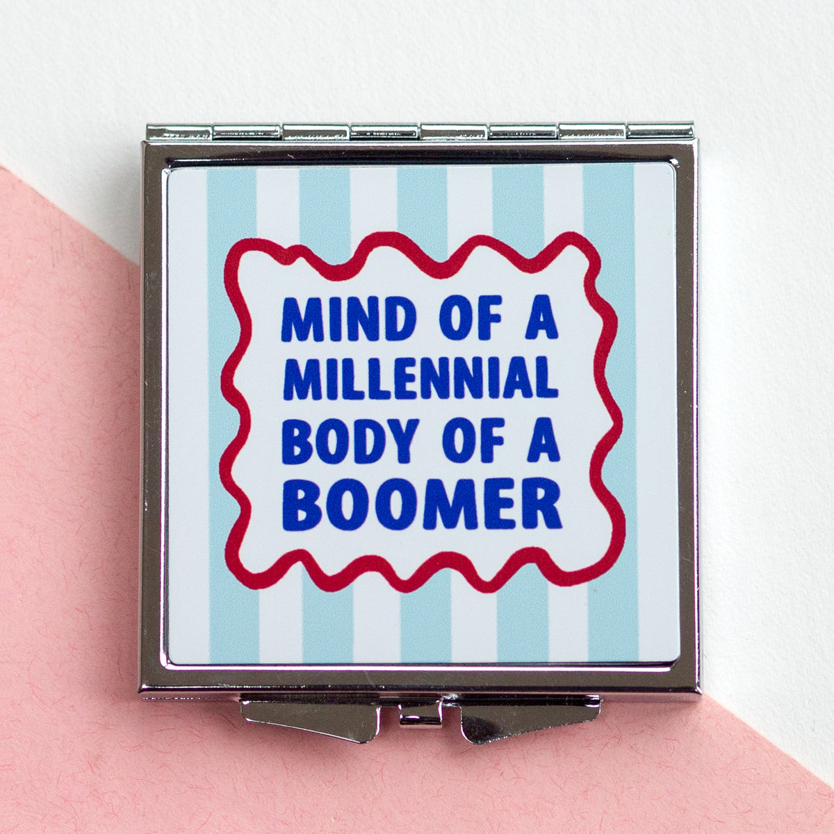 Compact mirror with 'Mind of a Millennial, Body of a Boomer' text on a striped background