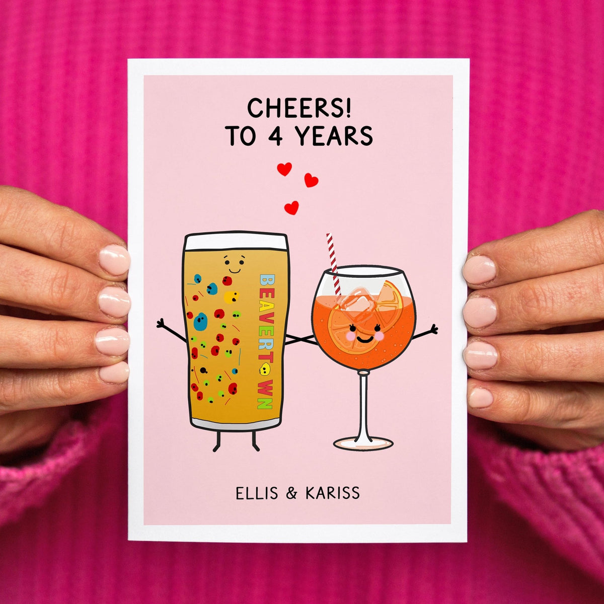 Anniversary card with cartoon drinks and 'Cheers! To 4 Years' text held by hands against a pink background