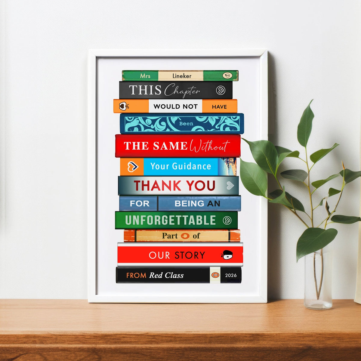 Framed print with colorful bookstack design on a wooden surface with a plant.