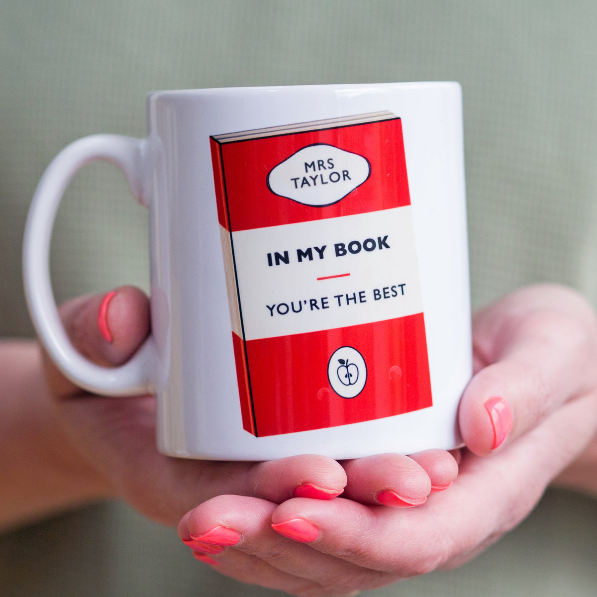White mug with red and white design held by hands with pink nail polish.