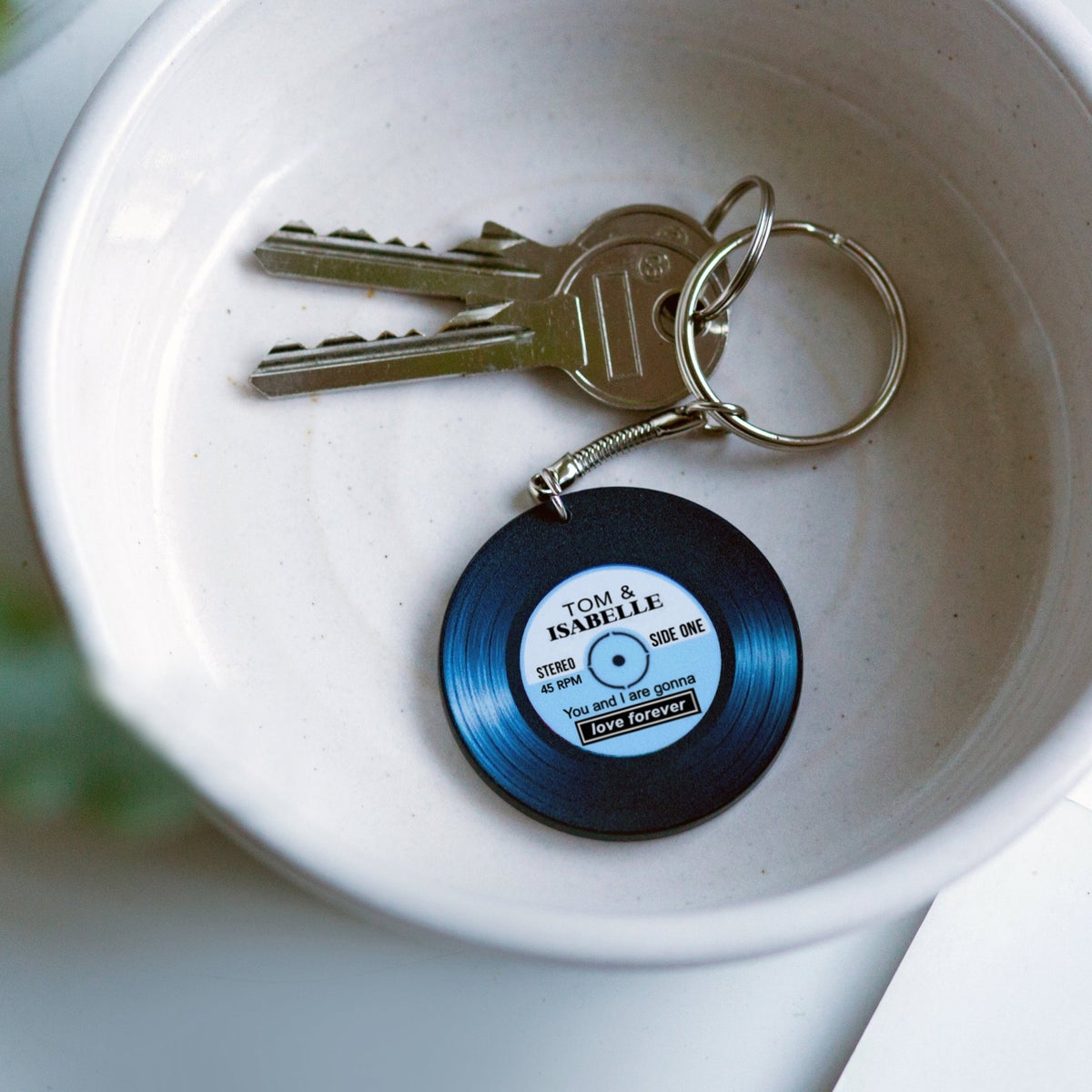 Keychain shaped like a vinyl record on keys with a white bowl in the background
