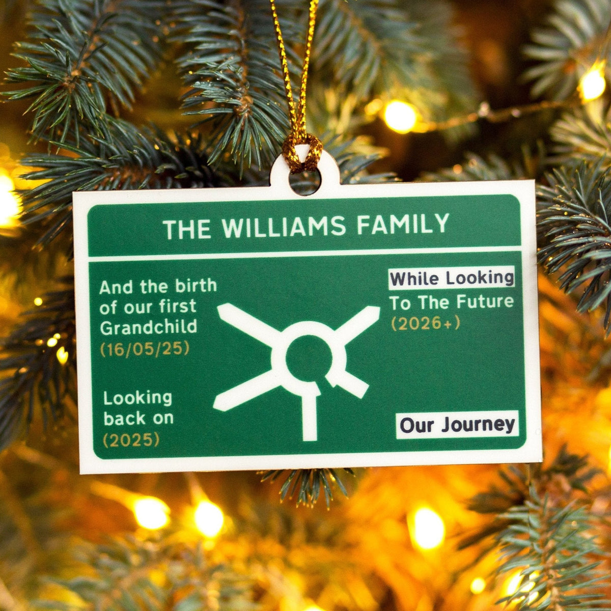Christmas tree ornament designed to look like a motorway road sign with 'The Williams Family' message on a tree with lights.