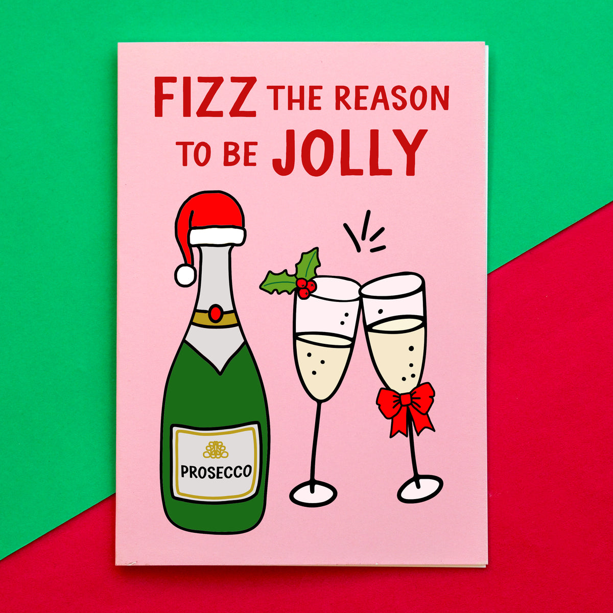 A pink Christmas card with the text 'FIZZ THE REASON TO BE JOLLY' and an illustration of a green Prosecco bottle, two clinking champagne glasses, and holiday accents, photographed against a green and red background.