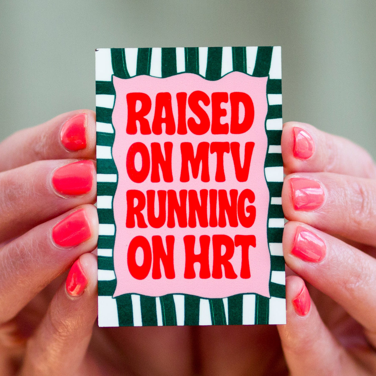 Hand holding a card with 'Raised on MTV Running on HRT' text against a blurred background