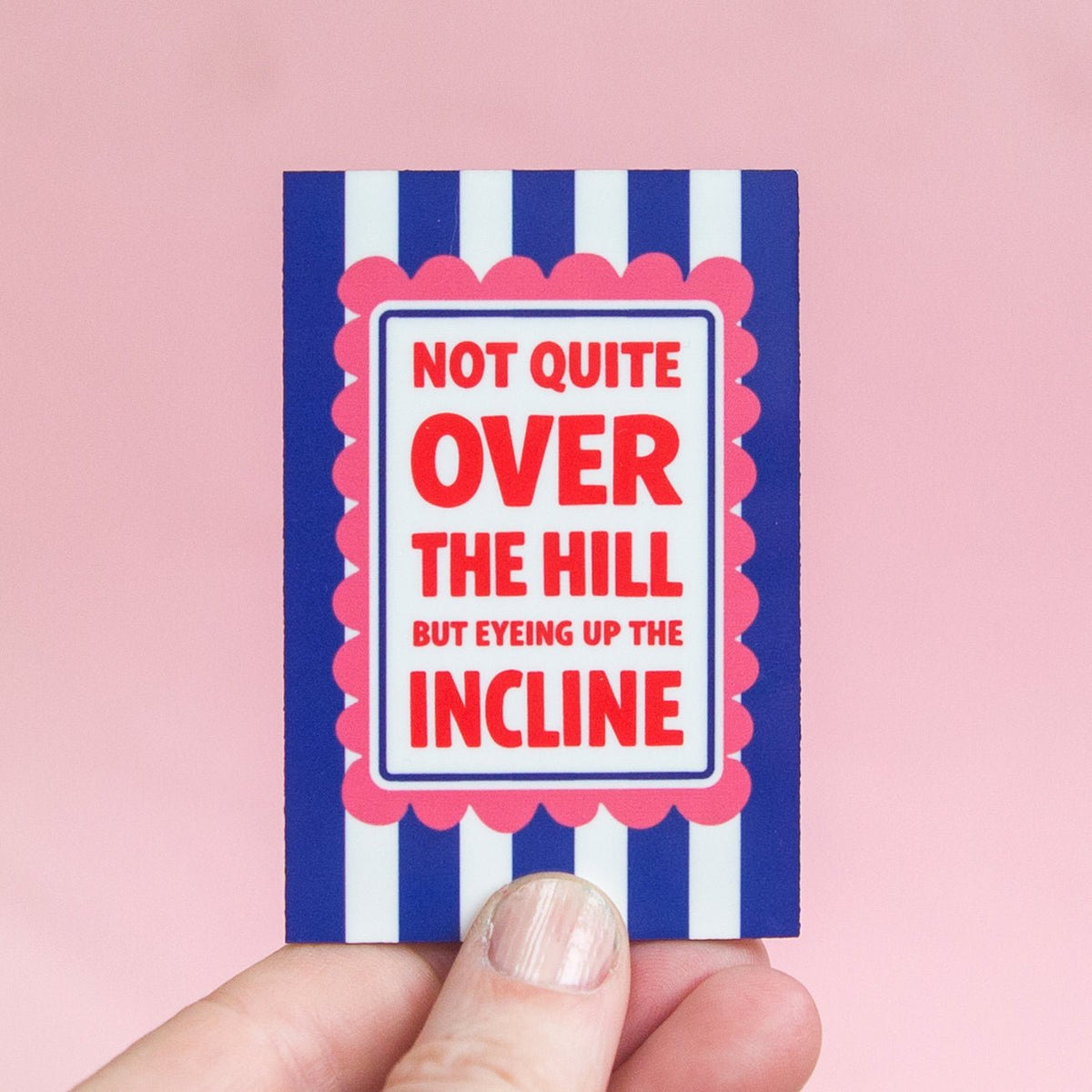 Fridge magnet with text 'Not quite over the hill but eyeing up the incline' held against a pink background