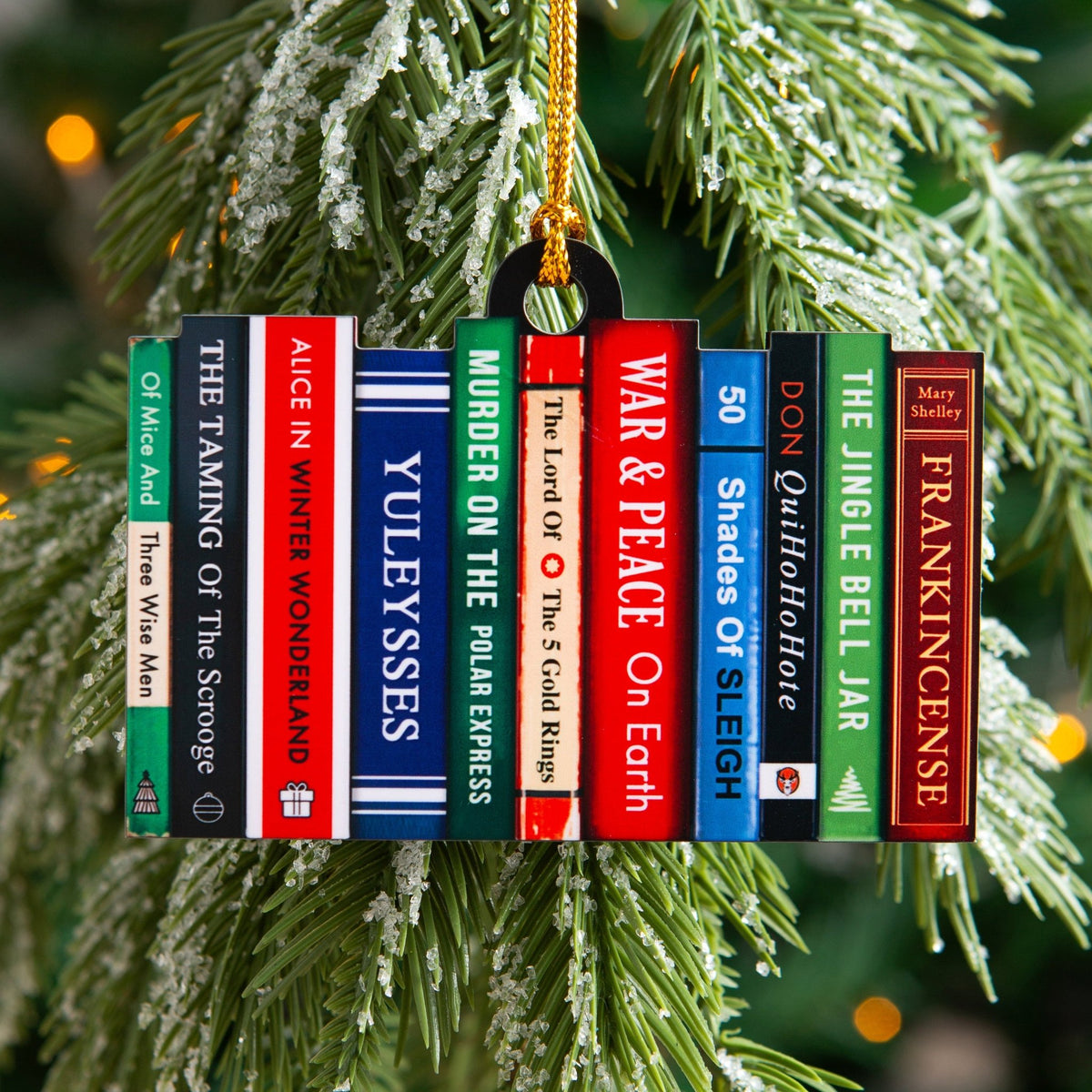 A Christmas ornament shaped like a row of colorful book spines with festive puns on classic novels as their titles, hangs from a gold string on a Christmas tree