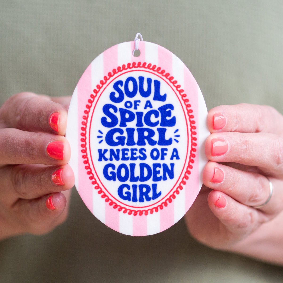Circular car air freshener with text 'Soul of a Spice Girl, Knees of a Golden Girl' held by hands.