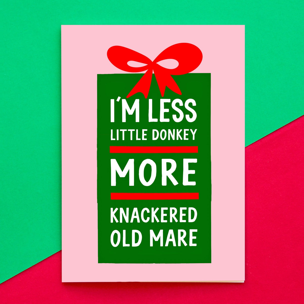 A square greeting card with a pink border and a green gift-box graphic topped with a red bow. The card has white text reading, 'I'M LESS LITTLE DONKEY MORE KNACKERED OLD MARE.