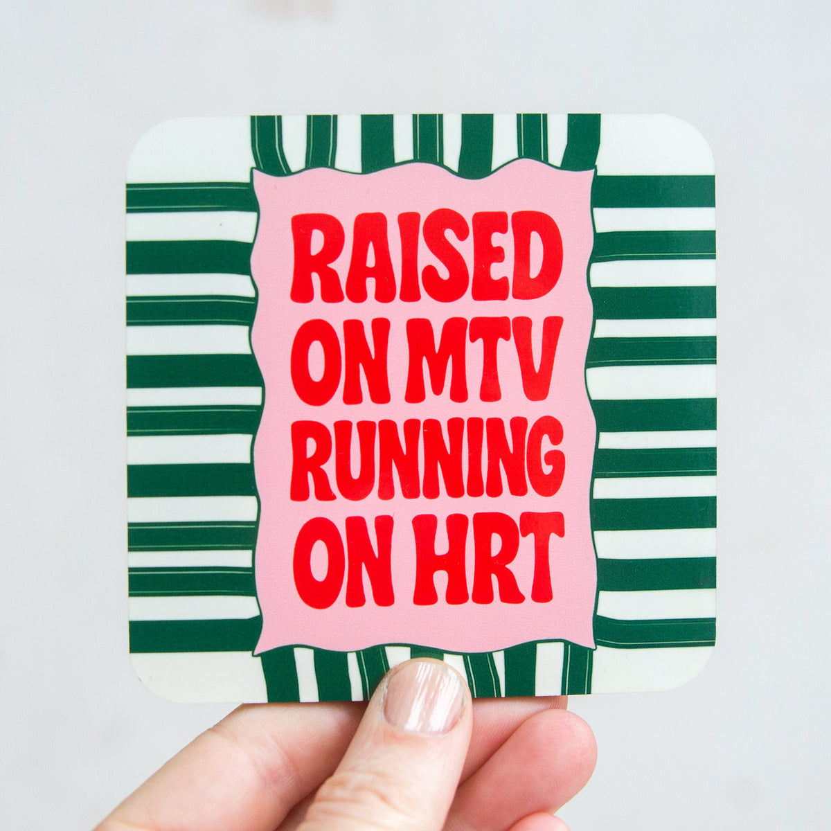 Sticker with text 'Raised ON MTV RUNNING ON HRT' on a green and white striped background held by a hand.
