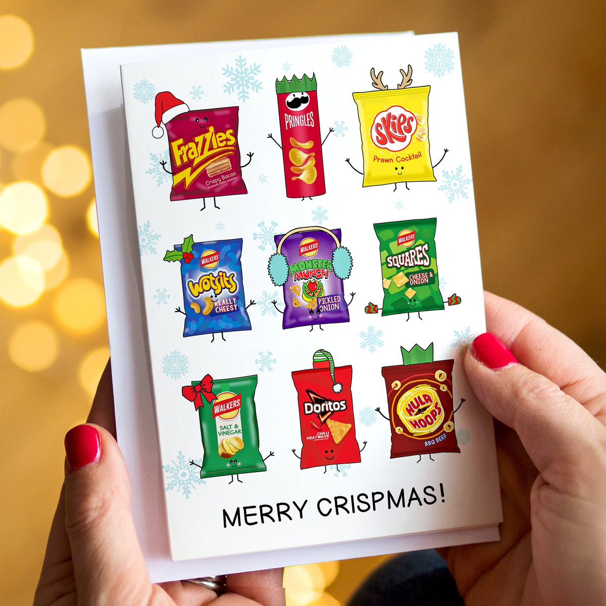 A person holds a Christmas card featuring cartoon illustrations of various crisp packets with the text 'MERRY CRISPMAS!'. The background is a warm, blurred golden bokeh.