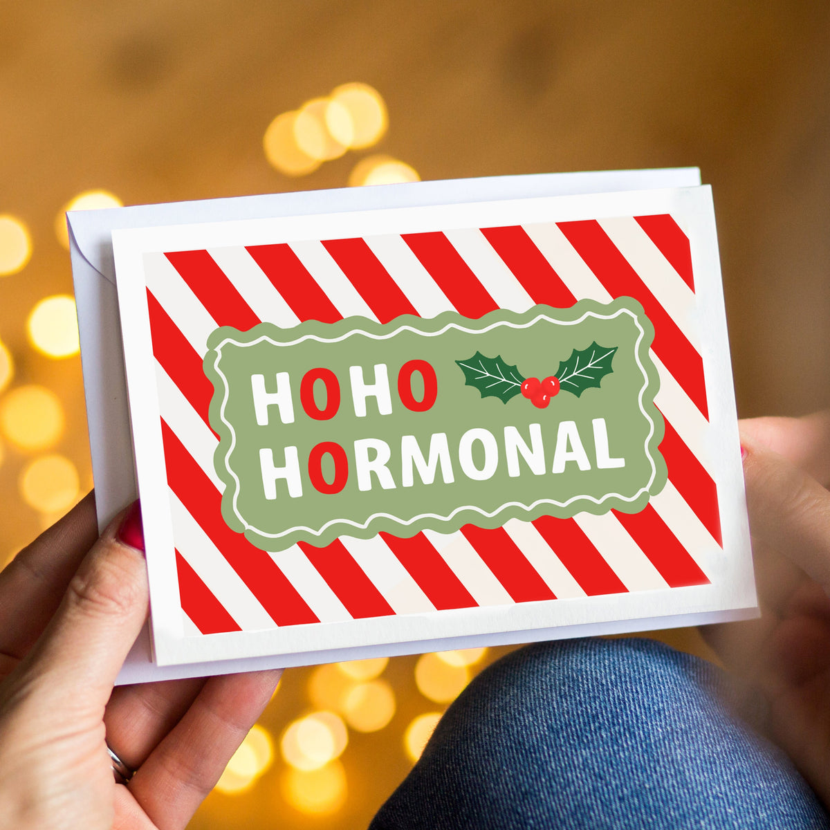 Card with 'HOHO HORMONAL' text held by a person against a blurred festive background