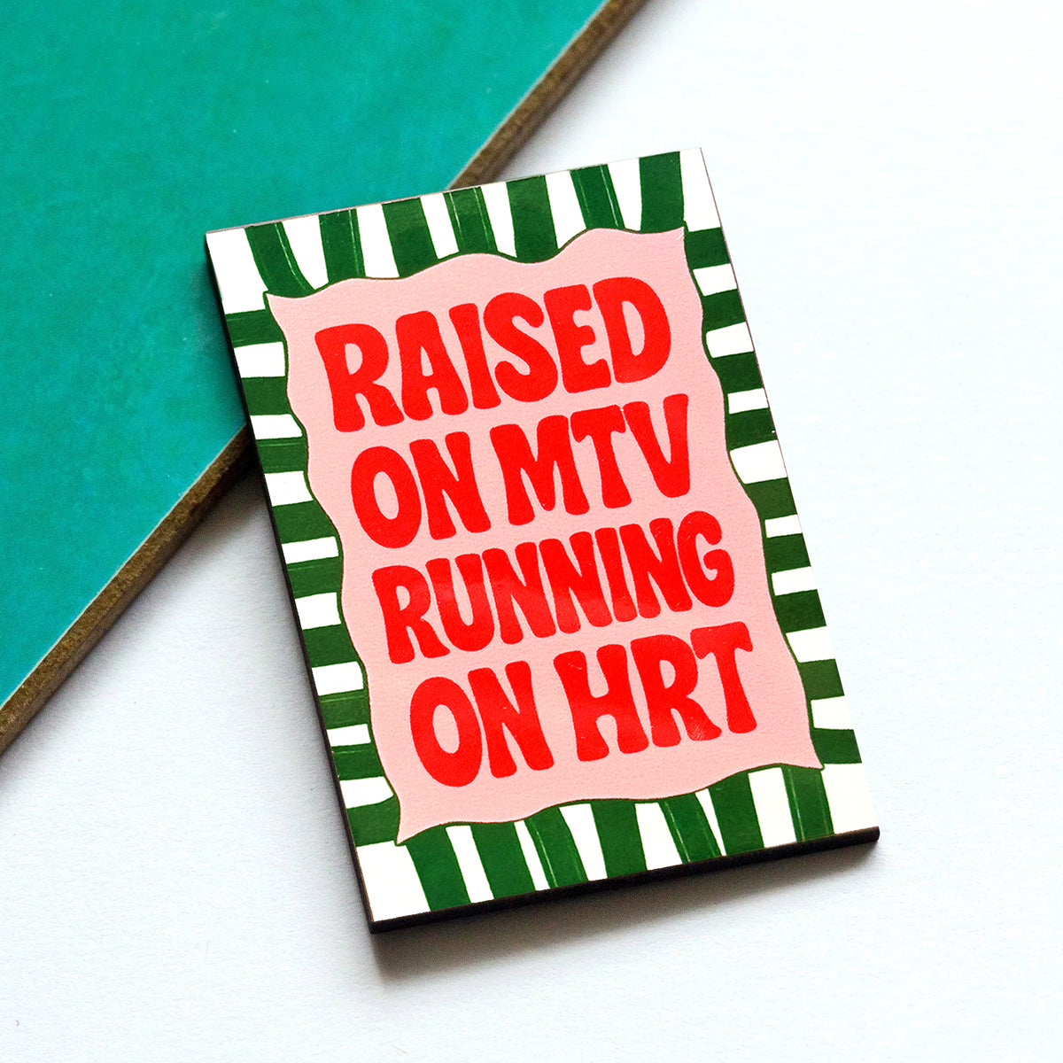 fridge magnet with text 'Raised on MTV Running on HRT' on a green and white striped background