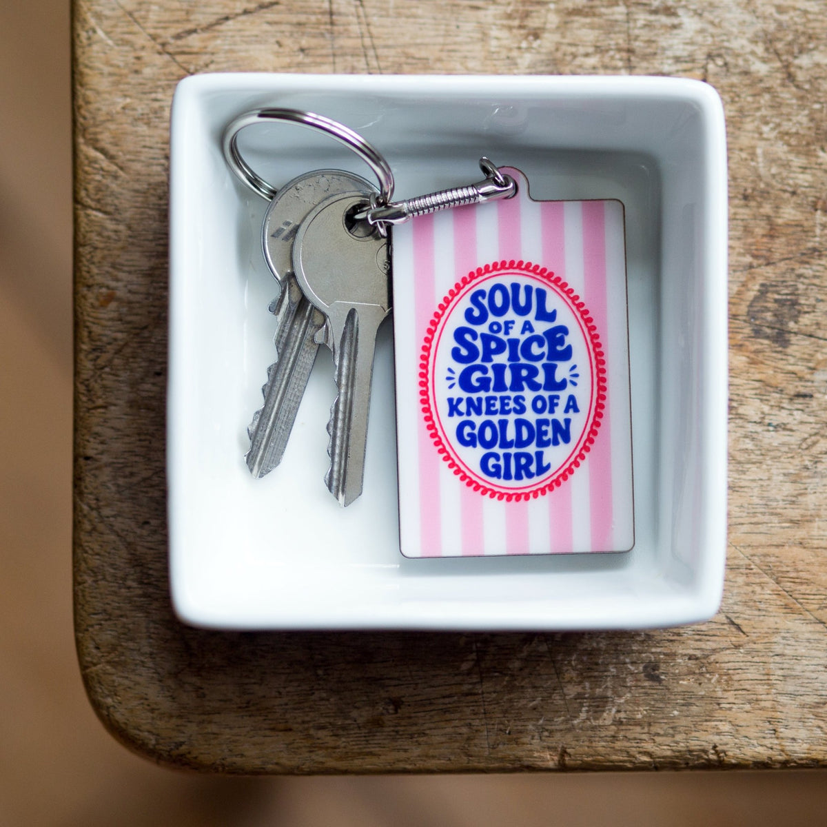 striped keyring with soul of a spice girl knees of a golden girl slogan in a white dish on wooden table