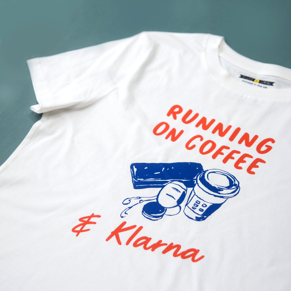 White t-shirt with 'Running on Coffee & Klarna' text and graphics on a gray background