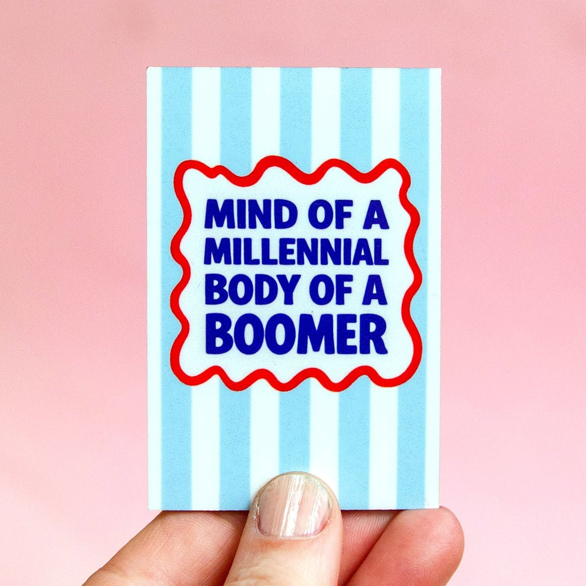 blue and striped magnet with slogan about aging held in a hand against a pink background