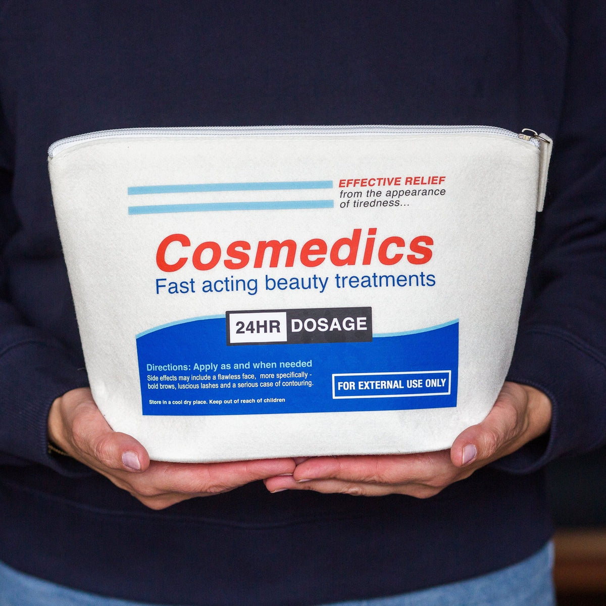 A person holding a white cosmetic pouch branded Cosmedics. The pouch has red and blue text and graphics, including 'Cosmedics', 'Fast acting beauty treatments', and '24HR DOSAGE'.