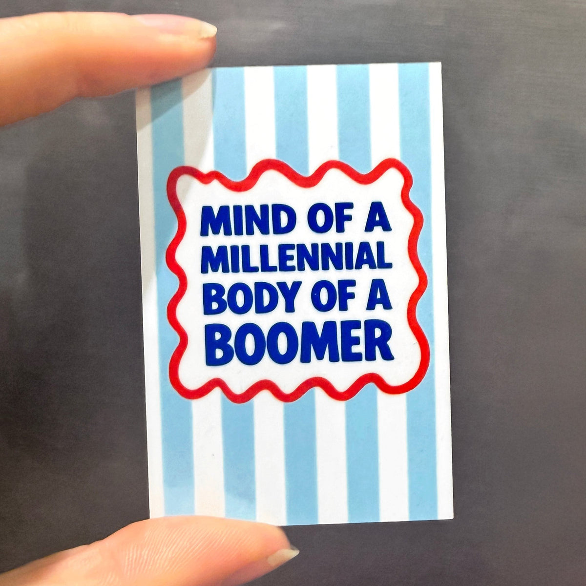 blue striped fridge magnet shown in hands  against a refrigerator with a funny slogan about middle age