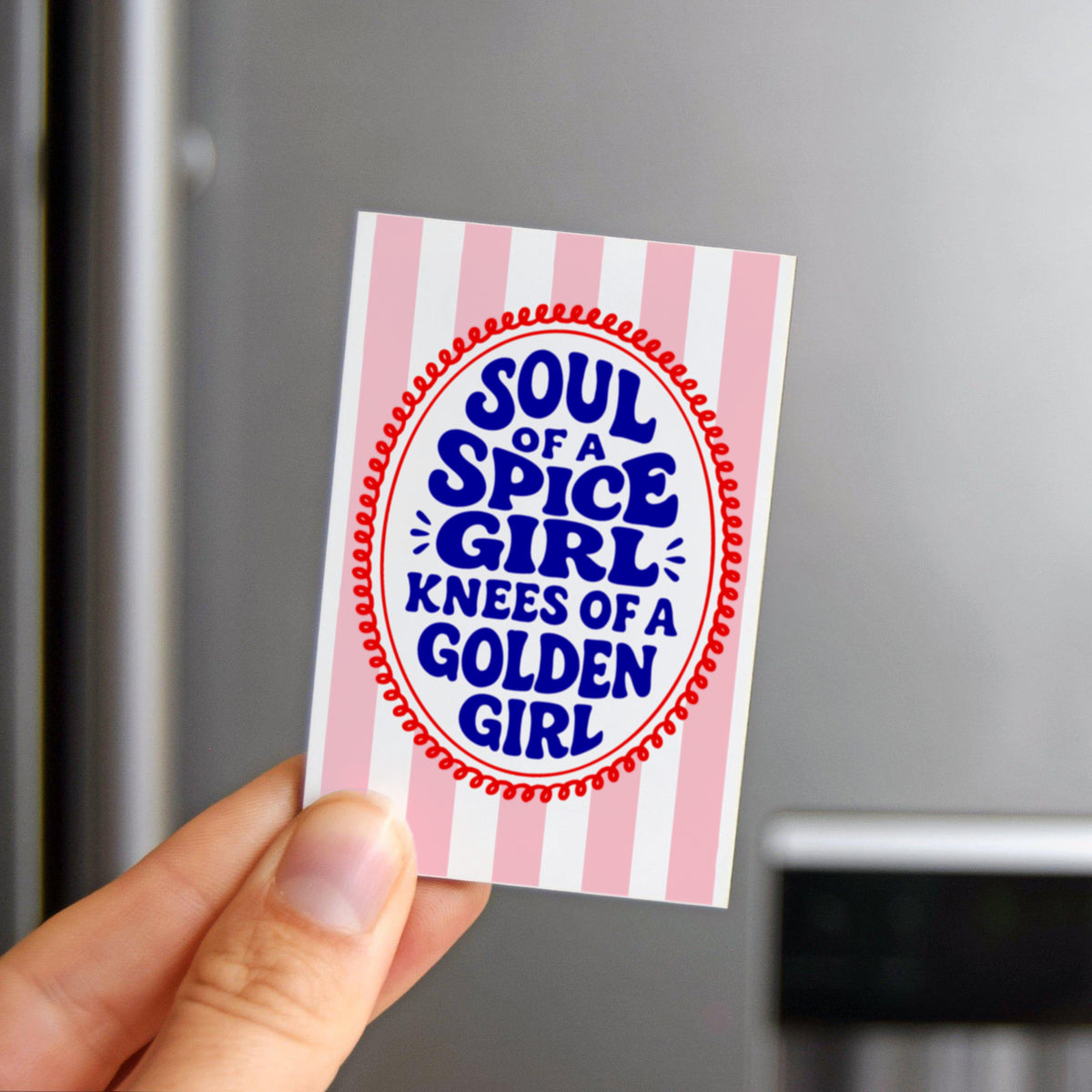 Hand holding a fridge magnet with striped border and text against a metallic refrigerator background
