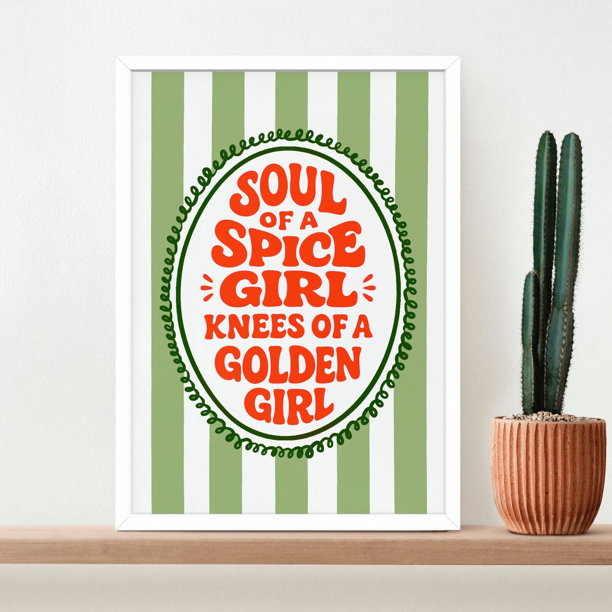striped slogan print in a white frame on a shelf with a cactus