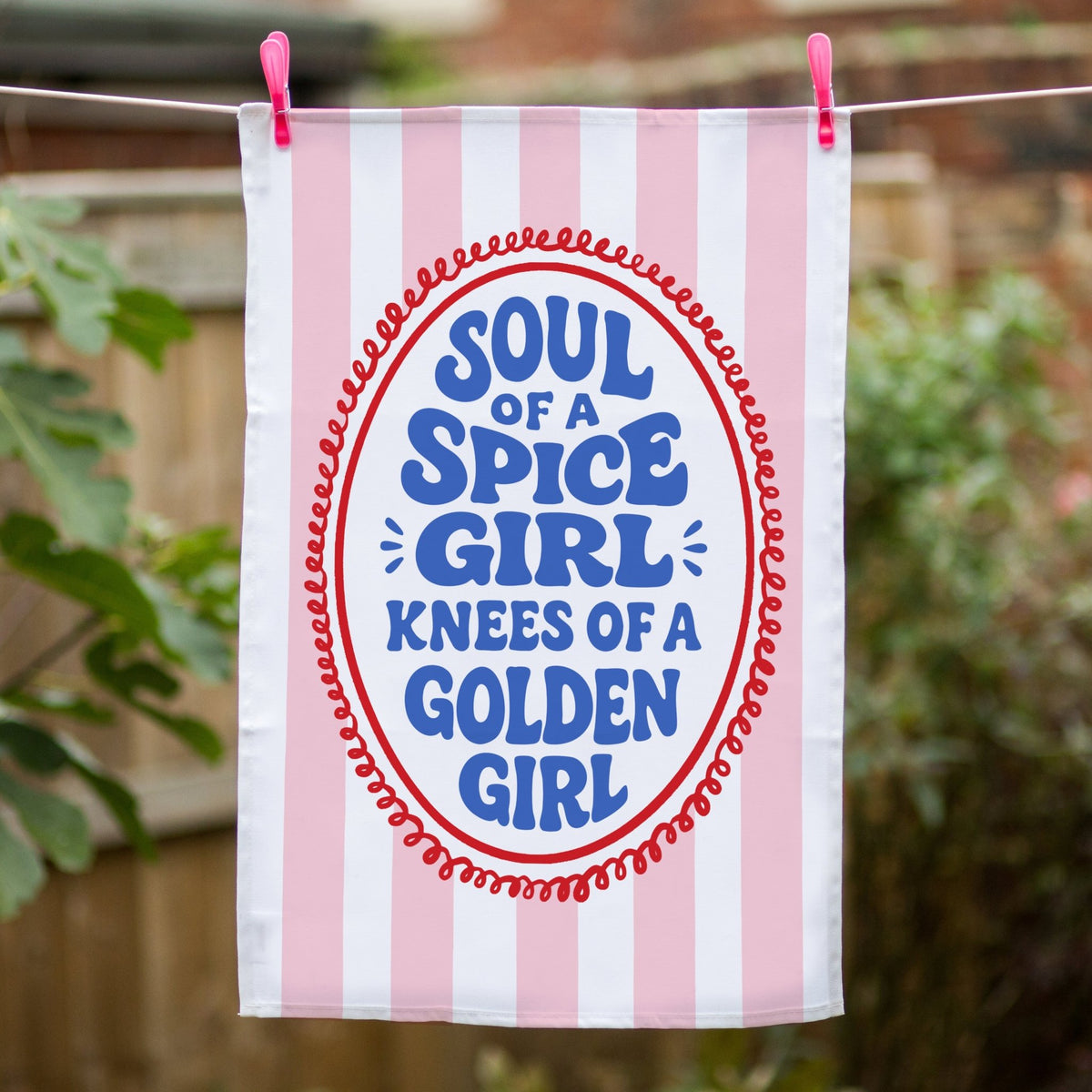funny tea towel with pink and white stripes and slogan hanging on a washing line outside
