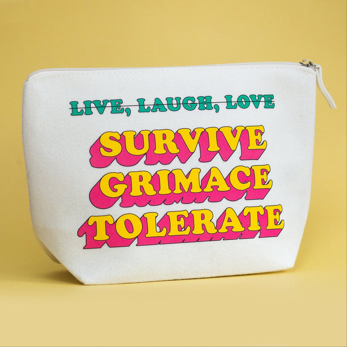 A white canvas zippered pouch with retro-style text reading 'LIVE, LAUGH, LOVE SURVIVE GRIMACE TOLERATE' in teal and pink/yellow lettering, set against a solid pale yellow background.