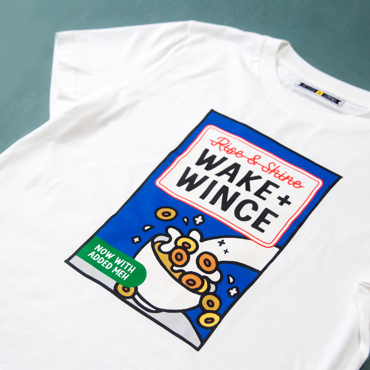 White t-shirt with 'Wake + Wince' graphic design on a gray background