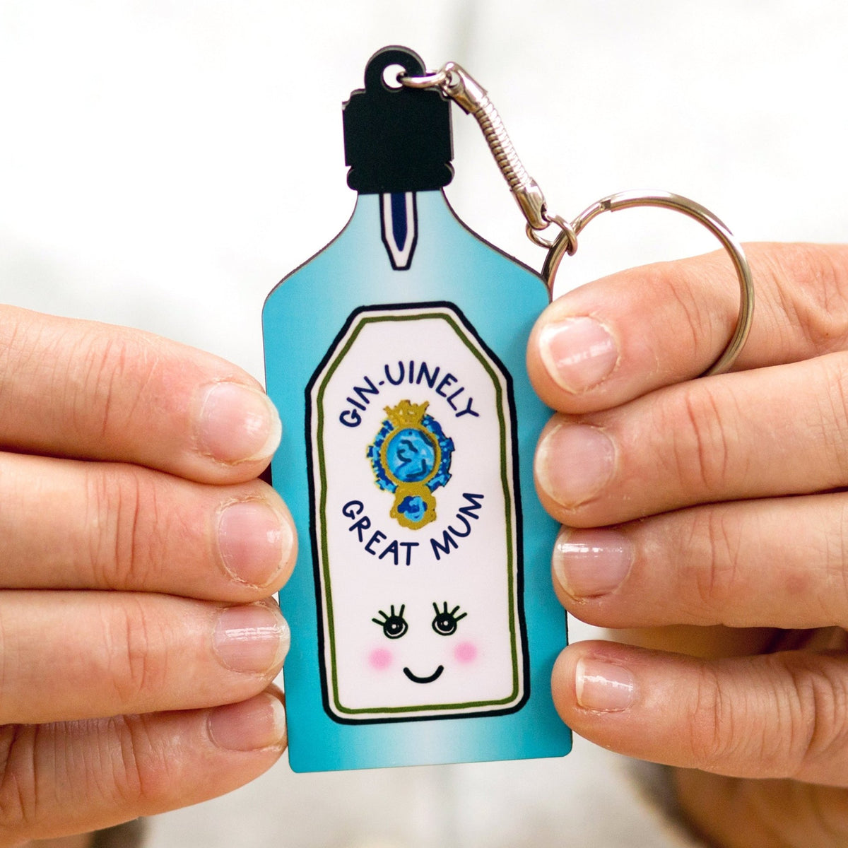 a keyring shaped like a gin bottle with the words 'Gin-uinely great mum' held in female hands