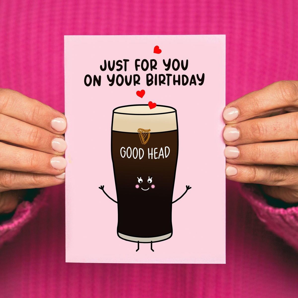Birthday card with a cartoon Guinness glass and text 'Just for you on your birthday Good Head' held by hands against a pink background.