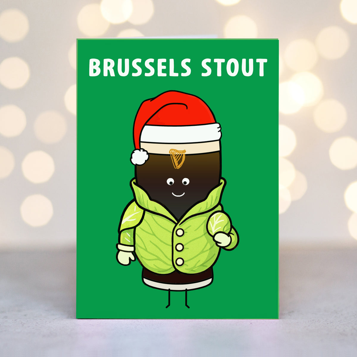 Card with a cartoon pint of guinnesswearing a Santa hat and brussels sprout costume on a green background with 'BRUSSELS STOUT' text.