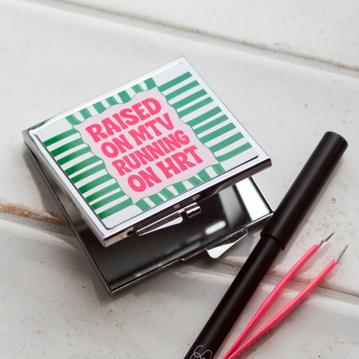 square compact mirror for women with green and white stripe design and the slogan raised on MTV running on HRT written in pink