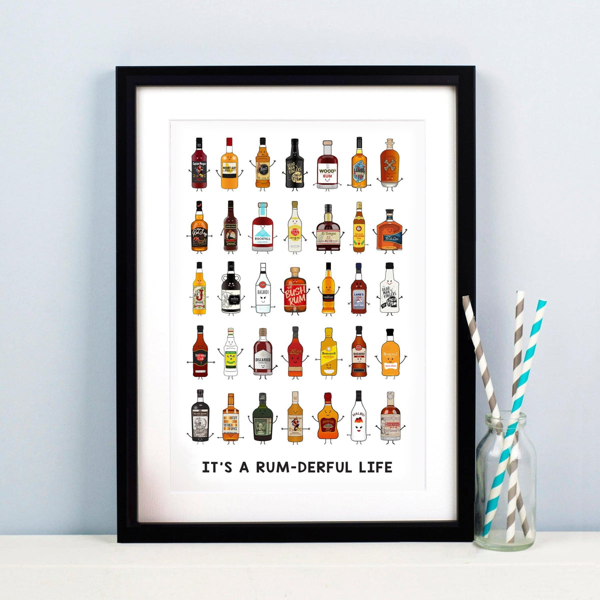Framed print with illustrations of rum bottles and 'It's a Rum-derful Life' text, next to a glass with straws.