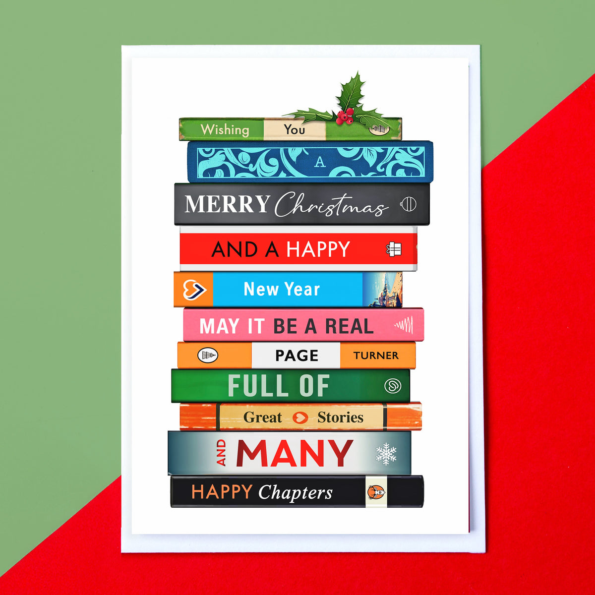 A white greeting card featuring a stack of colorful book spines with Christmas-themed phrases like 'Wishing You', 'Merry Christmas', and 'Happy Chapters'. The card is displayed against a diagonally split green and red background.